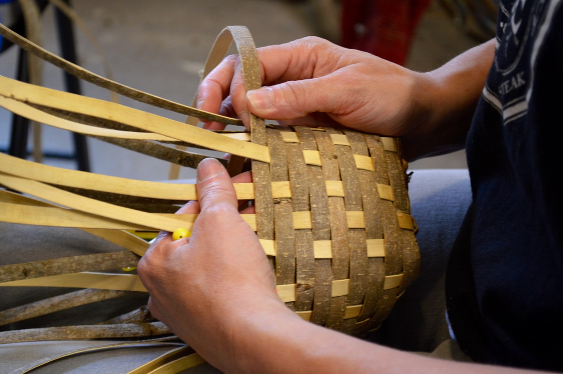 In a weaving class taught by Matt Tommey, a woman weaves bark into a basket.